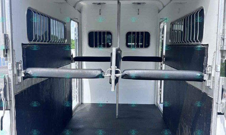 Interior of a white horse trailer with padded walls, metal partitions, and barred windows; empty with a diamond-plate rubber floor.