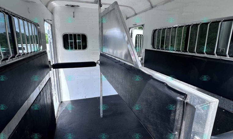 Interior of a horse trailer showing a divider in the center, with barred windows along the sides and diamond-plate flooring for traction.
