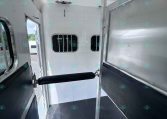 Interior of a horse trailer with a central dividing partition, diamond-plate floor, and sliding walls for transport.