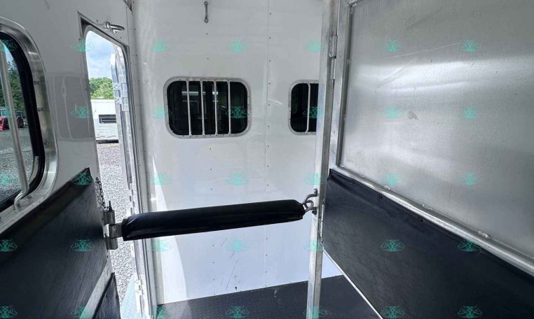 Interior of a horse trailer with a central dividing partition, diamond-plate floor, and sliding walls for transport.