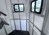 Interior of aluminum cargo trailer, corner view with two black-framed windows and diamond-plate floor.