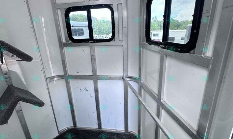Interior of aluminum cargo trailer, corner view with two black-framed windows and diamond-plate floor.