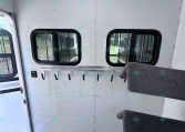 Interior of a silver trailer wall with two rectangular windows and a row of hooks beneath a rail.