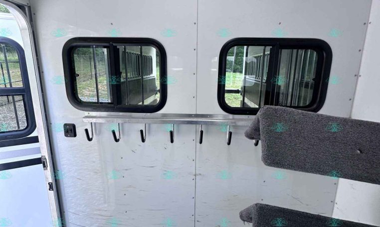 Interior of a silver trailer wall with two rectangular windows and a row of hooks beneath a rail.