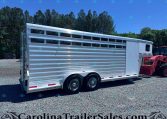 Silver aluminum livestock trailer with three axles parked on a gravel lot, trees in the background and a blue sky, watermark visible along the bottom edge.]
