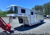 White gooseneck horse trailer with a chrome front, parked on a gravel lot with trees in the background.