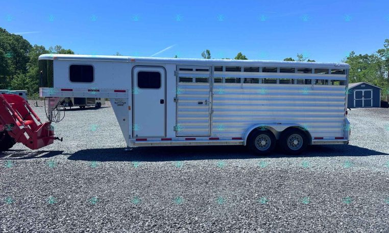 White, aluminum horse trailer with multiple windows and a gooseneck hitch on a gravel lot under a clear blue sky.