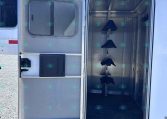Open horse trailer with metal interior and built-in stalls along the right wall, door wide open to the outdoors