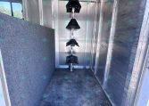 Interior of an aluminum trailer with a vertical rack holding several black hanging tack pieces along a central pole.