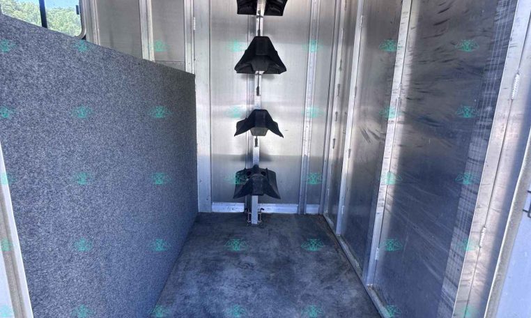Interior of an aluminum trailer with a vertical rack holding several black hanging tack pieces along a central pole.