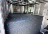 Interior of an empty aluminum cargo trailer with metal walls, ceiling rails, and a blue-gray carpeted floor; side window visible.