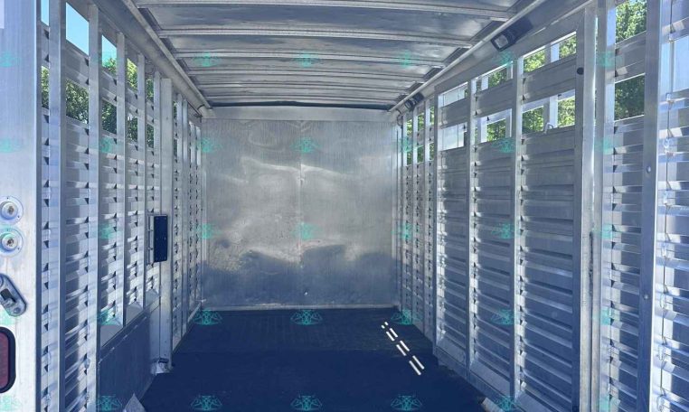 Interior of an empty aluminum livestock trailer with slatted sides and a black non-slip floor, daylight in from open doors