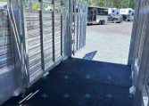 Interior of a metal trailer with ribbed aluminum walls, a black non-slip floor, and an open rear doorway; other trailers are visible outside in a gravel lot.