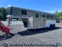 Large gray gooseneck horse trailer with living quarters, attached to a red tow hitch, parked on a gravel lot with trees in the background.