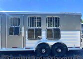 Silver Featherlite horse trailer side with barred windows, entry door, and dual wheels on pavement