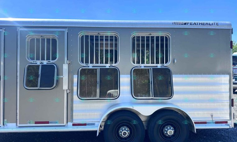 Silver Featherlite horse trailer side with barred windows, entry door, and dual wheels on pavement