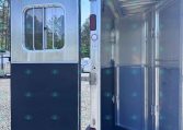 Open aluminum horse trailer with interior dividers visible and the side door swung open to the rear, showing the stall area.