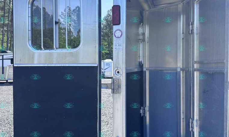 Open aluminum horse trailer with interior dividers visible and the side door swung open to the rear, showing the stall area.