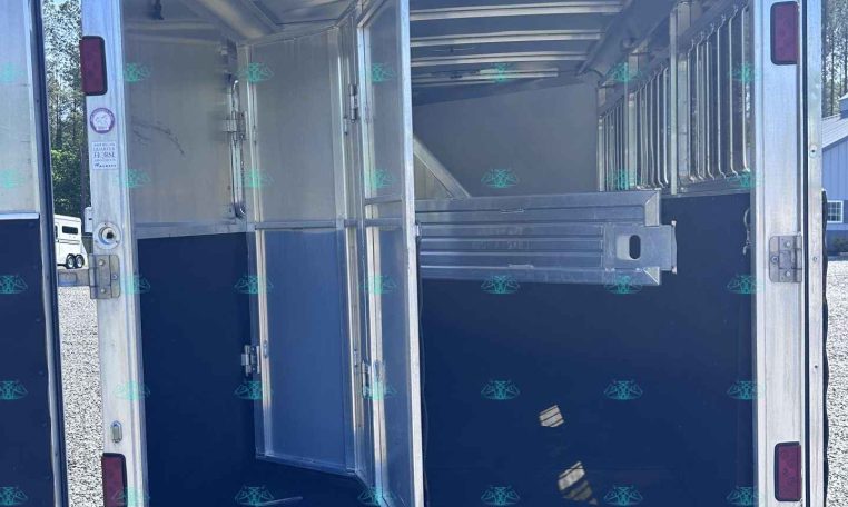 Rear view of an open aluminum horse trailer with divider and stalls, showing metal partition and blue interior walls for horses