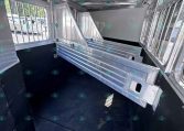 Interior of a metal horse trailer with partition stalls and barred windows, black rubber floor, and aluminum walls/ceiling.