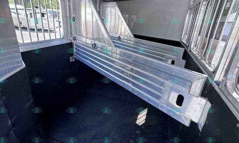 Interior of a metal horse trailer with partition stalls and barred windows, black rubber floor, and aluminum walls/ceiling.