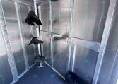 Interior of a silver cargo trailer with aluminum walls, vertical supports, and black seat frames mounted along the wall with a blue carpeted floor.