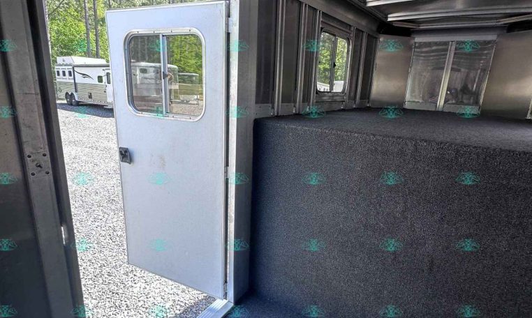 Interior view of a metallic trailer with a dark carpet, open door to outside, and windows along the side showing another trailer outside