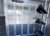 Interior of an aluminum trailer showing metal wall studs, a horizontal black plastic bracket, and a dark carpeted floor.