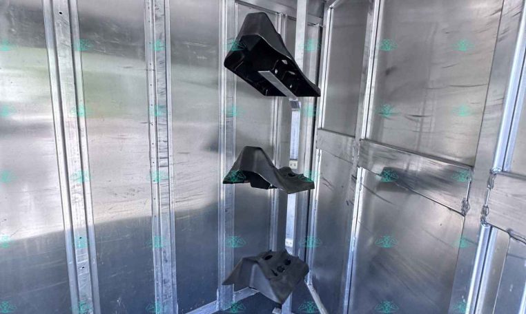 Interior of a silver aluminum trailer with vertical dividers and ceiling-mounted rails; black plastic supports or guards hang from a central post inside the trailer.