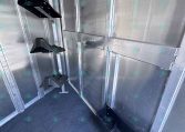 Interior of an aluminum trailer wall with black plastic wheel fenders hanging along the side; blue carpeted floor visible.