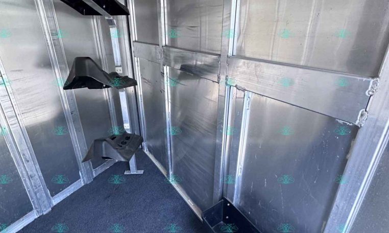 Interior of an aluminum trailer wall with black plastic wheel fenders hanging along the side; blue carpeted floor visible.