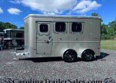 Silver aluminum horse trailer with three side windows parked on a gravel lot under a blue sky; branding reads 'Sportman' on the door side of the trailer.