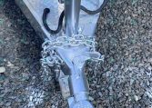 Close-up of a trailer hitch showing a silver diamond-plate trailer, safety chains, and a coupler at the tongue resting on gravel.