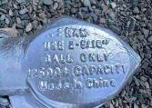Close-up of a metallic trailer lock resting on gravel, showing stamped specifications like 2-5/16 inches and 1500 lb capacity on the body.