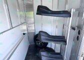 Interior of a metal trailer with two black contoured seats mounted along the wall and a wheel visible toward the back.