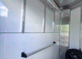 Interior view of a silver metal trailer with a row of hooks along the ceiling and a spare tire in the corner on a dark floor