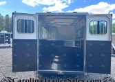 Open horse trailer with divider stalls visible inside, blue exterior and barred windows, parked on gravel.