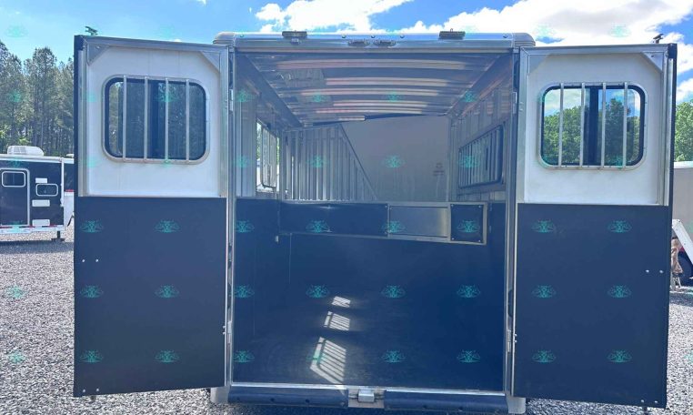 Open horse trailer with divider stalls visible inside, blue exterior and barred windows, parked on gravel.