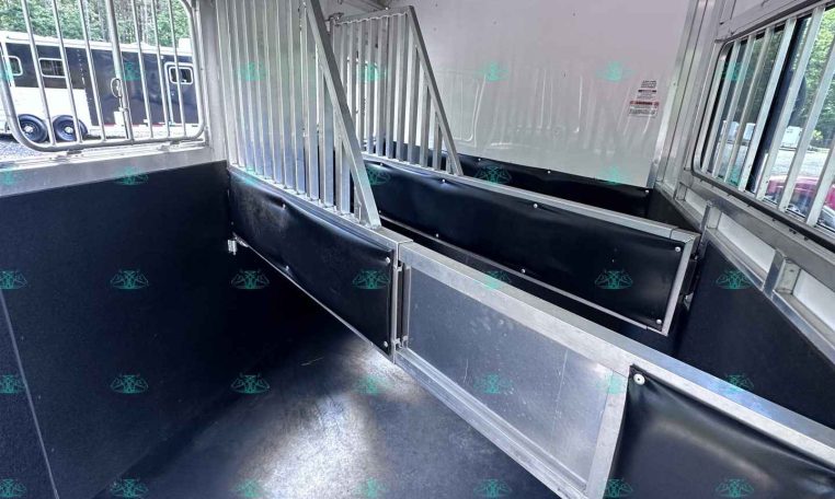 Interior of a metal horse trailer with divided stalls and black padding along the walls. Window bars along the side.