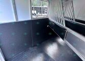 Interior of a metal trailer with vertical divider bars and a small window showing outside.