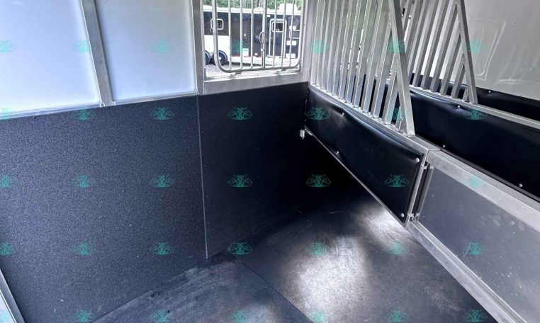 Interior of a metal trailer with vertical divider bars and a small window showing outside.