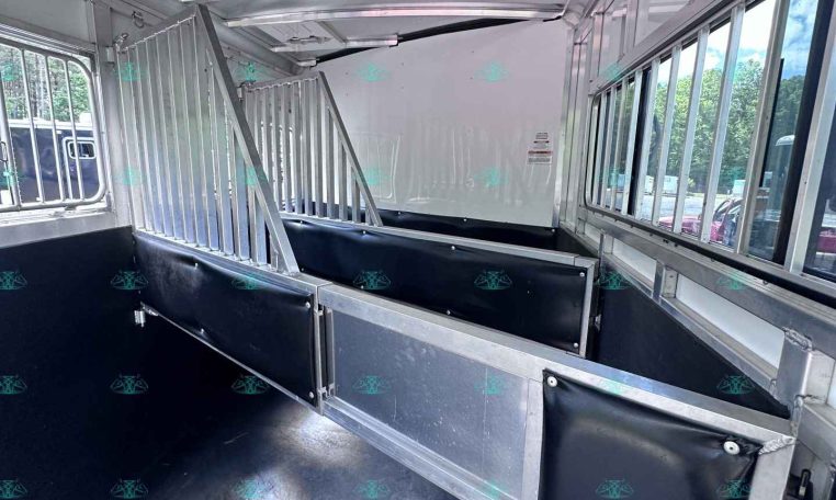 Interior of a aluminum horse trailer with divided stalls and padded side panels, view toward the back of the trailer