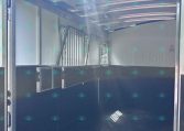 Interior of a horse trailer with partitioned stalls and metal bars, door open to the outside light.