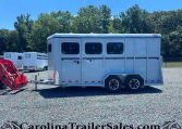 White horse trailer on a gravel lot with trees in the background and other trailers nearby, under a clear blue sky.