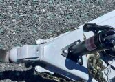 Close-up of a trailer hitch with safety chains attached to a grey metal frame on a gravel surface.
