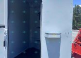 Open side door of a light-gray utility trailer revealing an empty interior on a sunny day