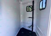 Interior of a small gray trailer with a vertical black post and a fold-out metal rack; two side windows.