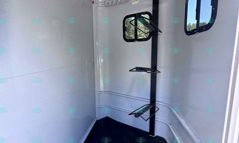 Interior of a small gray trailer with a vertical black post and a fold-out metal rack; two side windows.