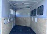 Empty trailer interior with wood-paneled sides, windows along the right, and a low ramp at the back; dark non-slip floor visible.
