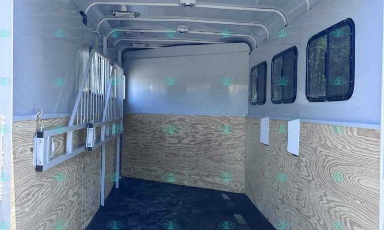 Empty trailer interior with wood-paneled sides, windows along the right, and a low ramp at the back; dark non-slip floor visible.